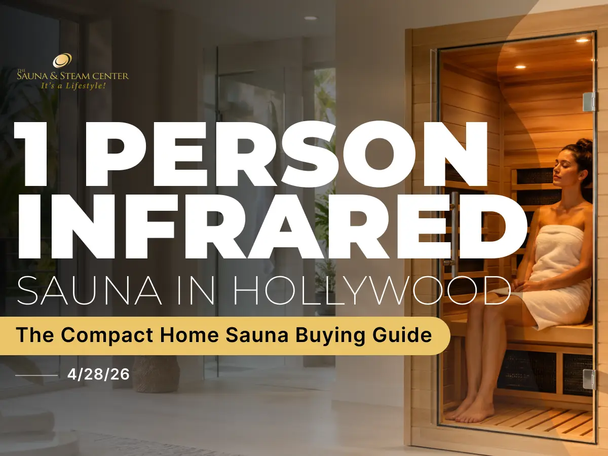 A compact one-person infrared sauna in a bright, modern home with warm interior lighting. A person sits inside the sauna relaxing on the bench.